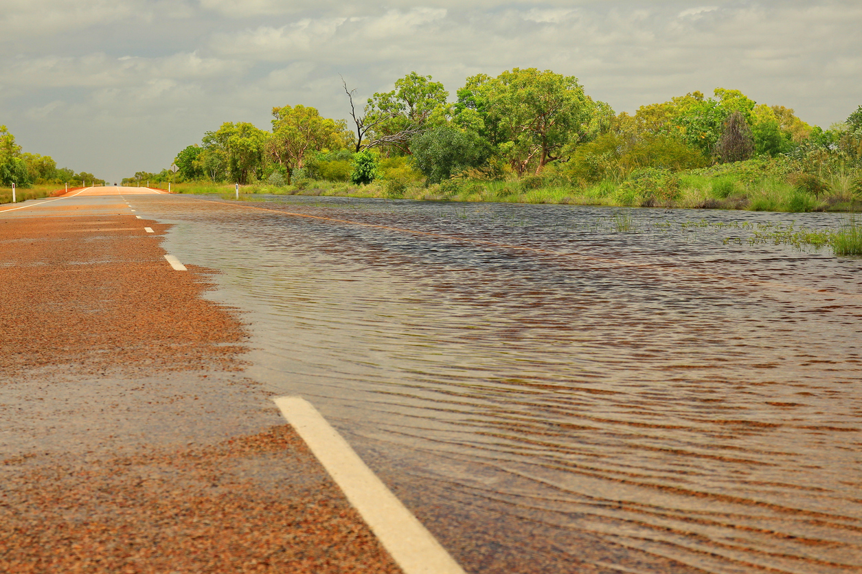 A red road in the outback is half covered by flood water.