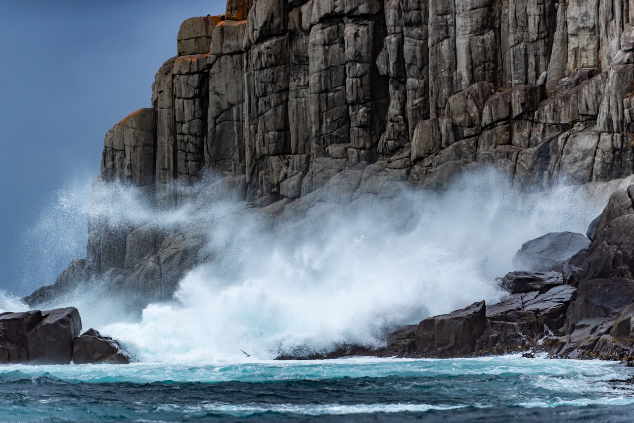 Waves crash into a large rocky cliff.