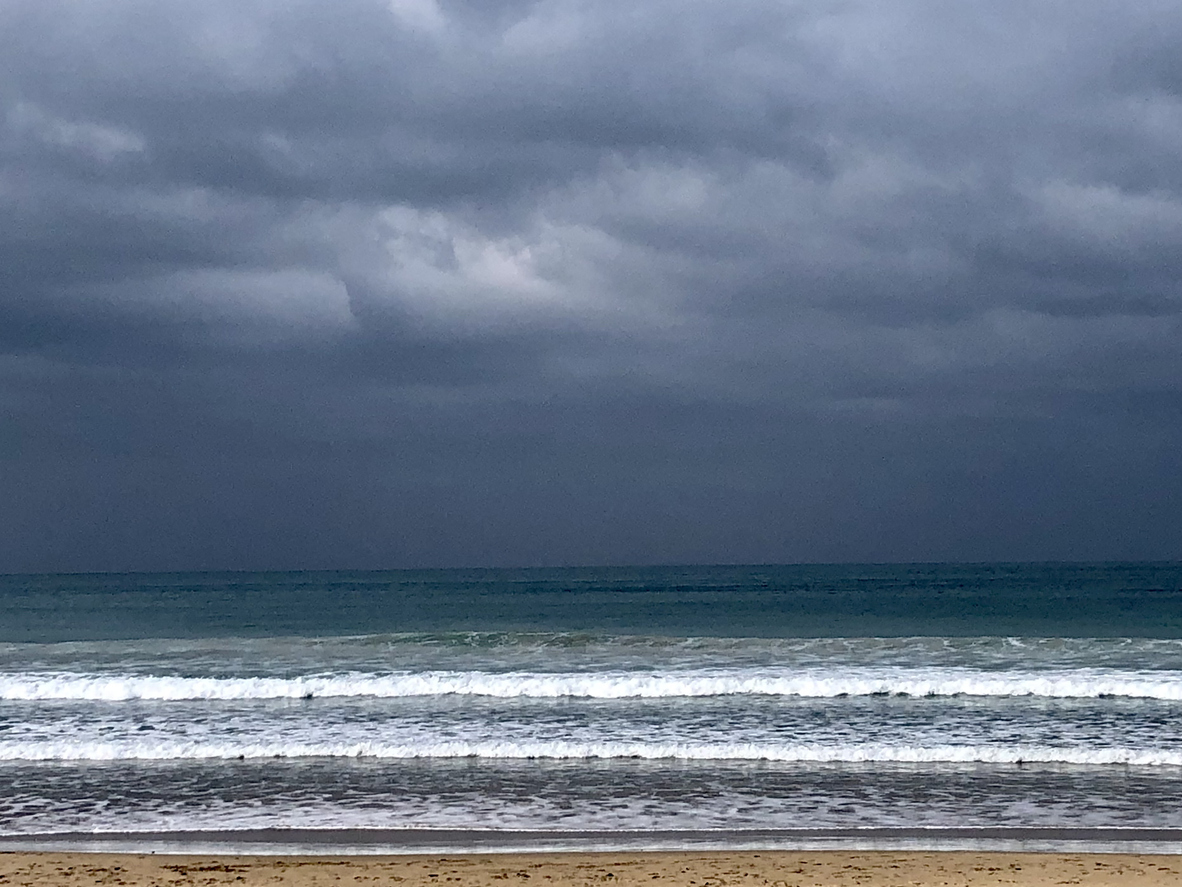 A dark sky is visible above the ocean with small waves rolling into a sandy shore.