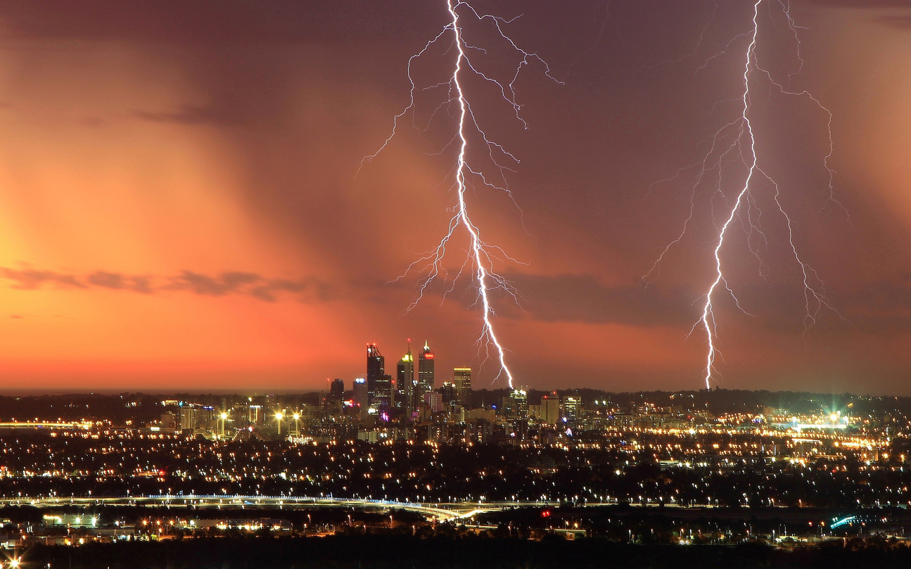 Two lightning strikes appear on a red strike striking down to a cityscape at night below.