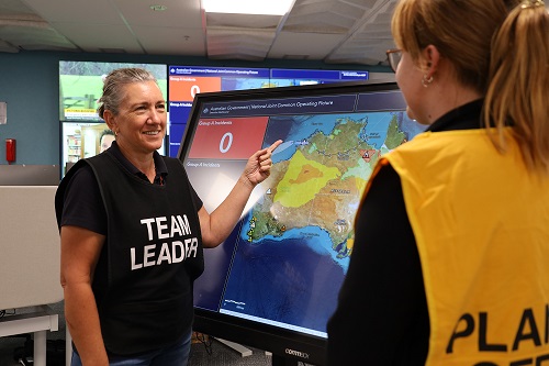 A person in a black top with white "Team Leader" written on it is standing in front of an incident map of Australia.