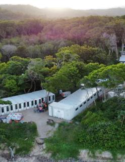 Two white emergency temporary housing units sit amongst green trees in a bushland area. 