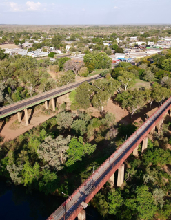 An aerial view of a landscape featuring two elevated bridges crossing over a green, wooded area. The bridges run parallel to each other and appear to be constructed of concrete and steel. 