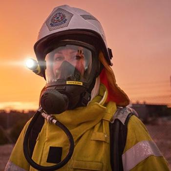 A person wearing hazmat equipment stands in front of an orange sky.