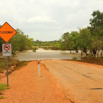 A flooded road in outback Australia with water covering the red dirt.