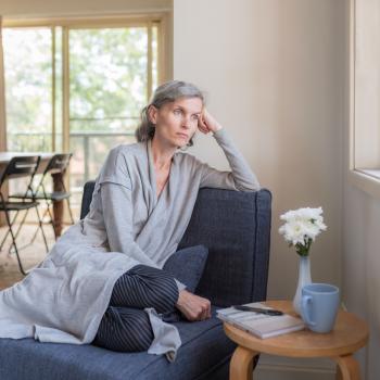 A woman sits on a chair while looking out a window.