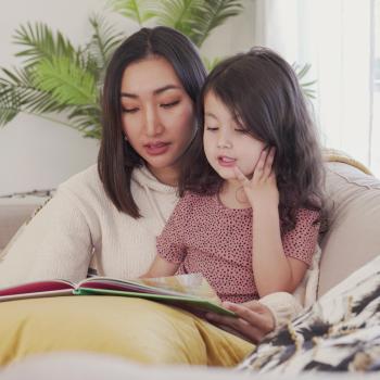 A woman and young child sit on a couch reading a book.