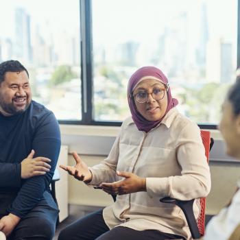 Three people sit in an office space having a discussion.