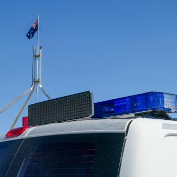 The Australian Flag above Parliament House with a police car in foreground.