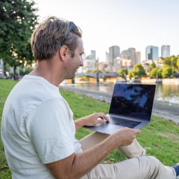 A man sits by the river in Melbourne working on a laptop.