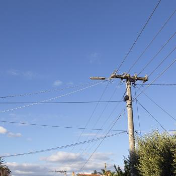 A telephone pole with lines going in all directions set in front of a blue sky.