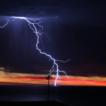 A lightning strike hits an antenna. A red and orange sunset is visible below storm clouds.