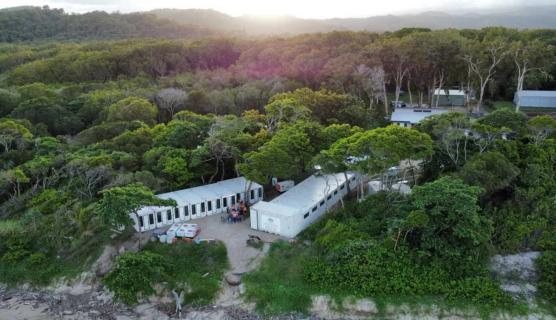 Two white emergency temporary housing units sit amongst green trees in a bushland area. 