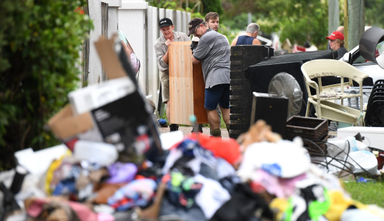 Two men are carrying a chest of draws found on the street during a post storm clean up. Trash and other damaged household items are scattered on the street.