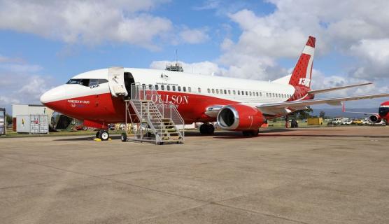 A red and white plane is parked on a runway. A white ladder pf stairs is descends down at the front of the plane with the front door is open.