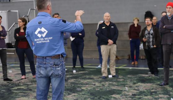 A person wearing a Disaster Relief Australia uniform stands with others on a large map covering the floor.