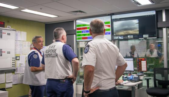 A state response controller wearing a vest works in a control room with multiple screens.