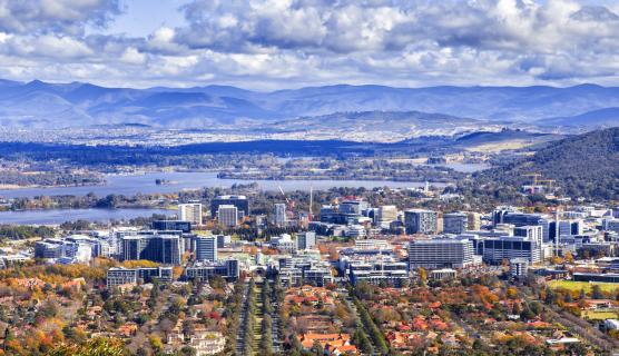 An aerial image of a town with tree lined streets going into a city and mountains in the distance.