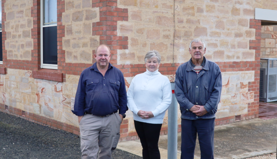 Three people stand in front of a refurbished brick community hall.