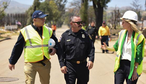 A group of men wearing safety vests and hard hats walking together on a road, surrounded by trees.