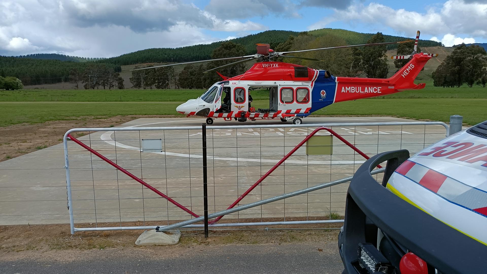 concrete helipad behind a fence in foreground with red and white helicopter in background