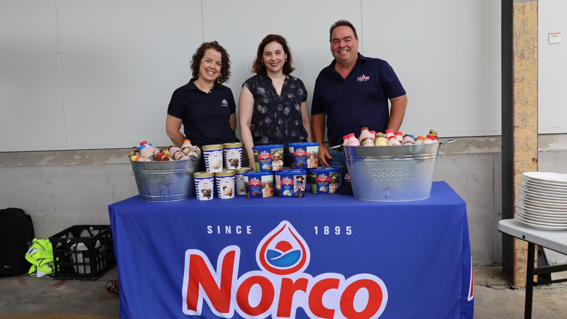 Three people stand behind a Norco branded table featuring ice cream and flavoured milk products.