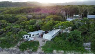 Two white emergency temporary housing units sit amongst green trees in a bushland area. 