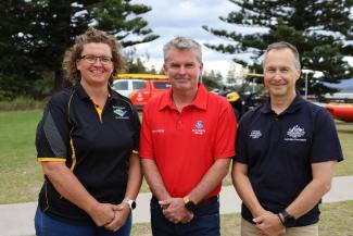 Three uniformed people pose for a photo outside a surf lifesaving club.