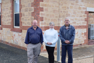 Three people stand in front of a refurbished brick community hall.