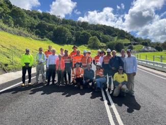 A group of people, some in high visibility workwear, pose for a photo in the middle of a new road.