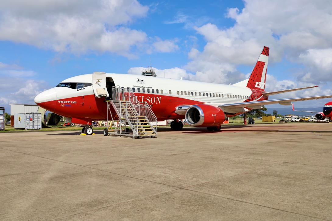 A large red and white plane sitting on the tarmac with stairs leading to its open entryway.